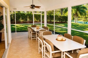 A dining area with a table and chairs, large windows, and a ceiling fan.