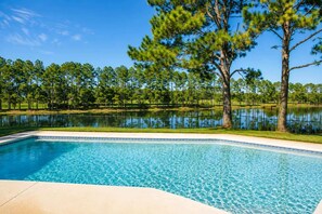 A swimming pool with clear blue water, surrounded by a grassy area and trees.