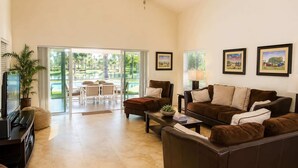 A living room with a sofa, coffee table, TV, and a dining area with a table and chairs. - SWISS 24 - Lake Stephanie (Clermont)