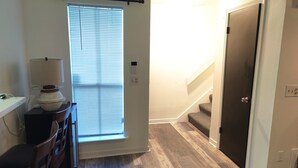 A hallway with a door, a window with blinds, a lamp, and a chair. - Charming NOLA Condo (New Orleans)