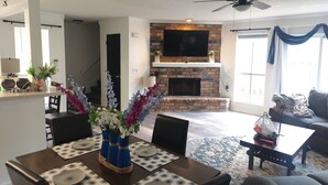 A dining area with a brick fireplace, a flat-screen TV above it, and a modern ceiling fan. - Charming NOLA Condo (New Orleans)