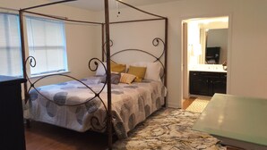 A four-poster bed with a patterned bedspread, a ceiling fan, and a view of a bathroom through an open door. - Charming NOLA Condo (New Orleans)