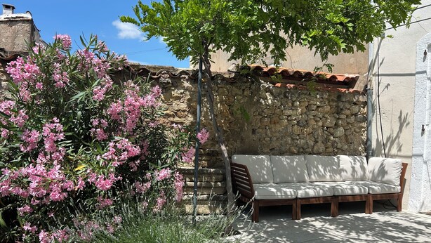 A stone wall, a bench, and pink flowering plants.