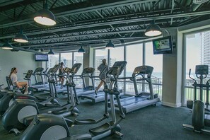 A gym with treadmills, weight machines, and large windows offering a city view.