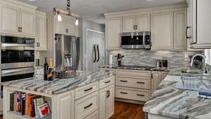 A modern kitchen with marble countertops, stainless steel appliances, and light-colored cabinetry. - Expansive Retreat with Heated Pool & Gorgeous Views (Cullman)
