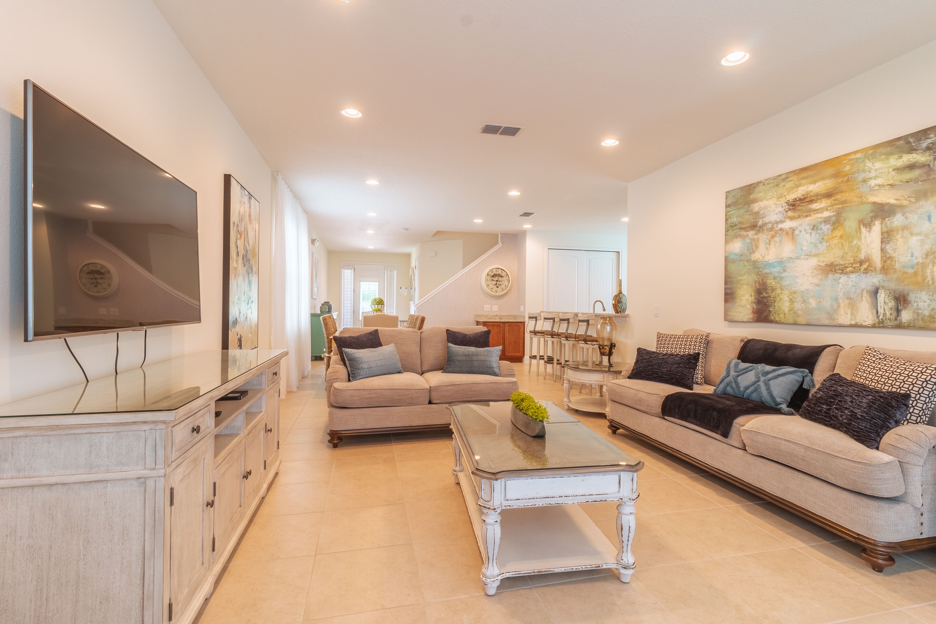 A spacious living room with a large flat-screen TV, a sofa, a coffee table, and a dining area with chairs and a table.