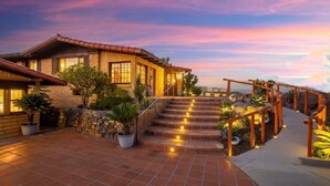 Una casa a due piani con facciata in mattoni, un patio piastrellato e una scala in legno con ringhiere.