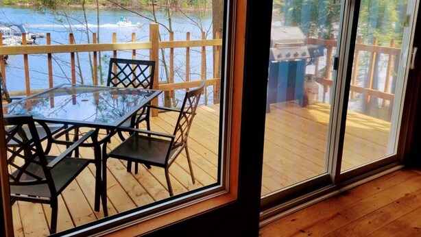 A wooden deck with a glass door leading to a view of a lake and dock. - Lakefront Muskoka Good View cottage (Gravenhurst)