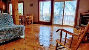 A spacious living room with a patterned sofa, wooden rocking chairs, and a dining area with chairs. Large windows provide natural light and a view of the outdoors. - Lakefront Muskoka Good View cottage (Gravenhurst)