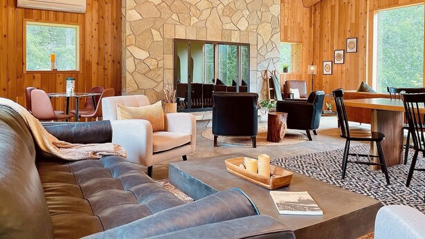 Una sala de estar acogedora con chimenea de piedra, paredes de madera y un ventanal con vistas a la vegetación.