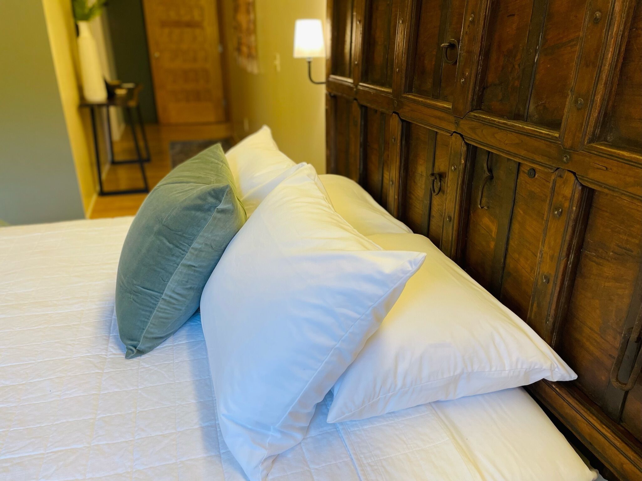 A bed with white and green pillows, a wooden headboard, and a wall-mounted lamp.