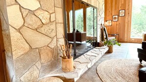 Una chimenea de piedra con puerta de cristal, un banco de madera y un ventanal con vistas a un bosque.