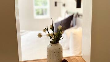 A small, white, polka-dotted vase with flowers on a wooden shelf, viewed through an arched window.