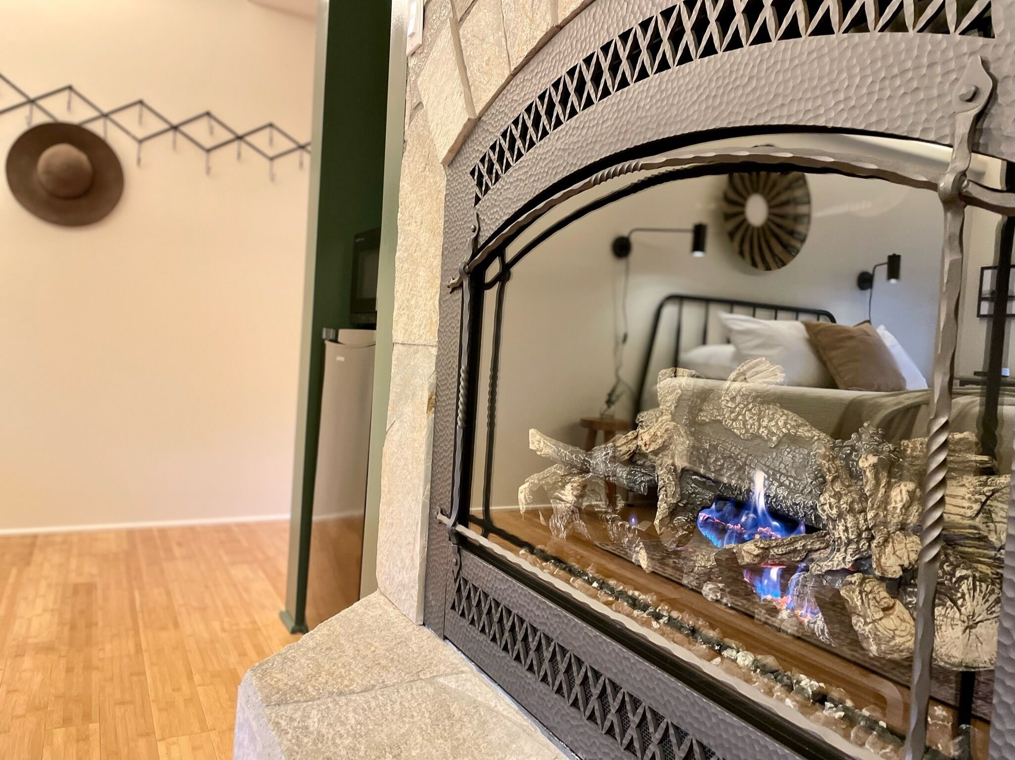 Una chimenea con frente de vidrio decorativo y una cama visible al fondo.
