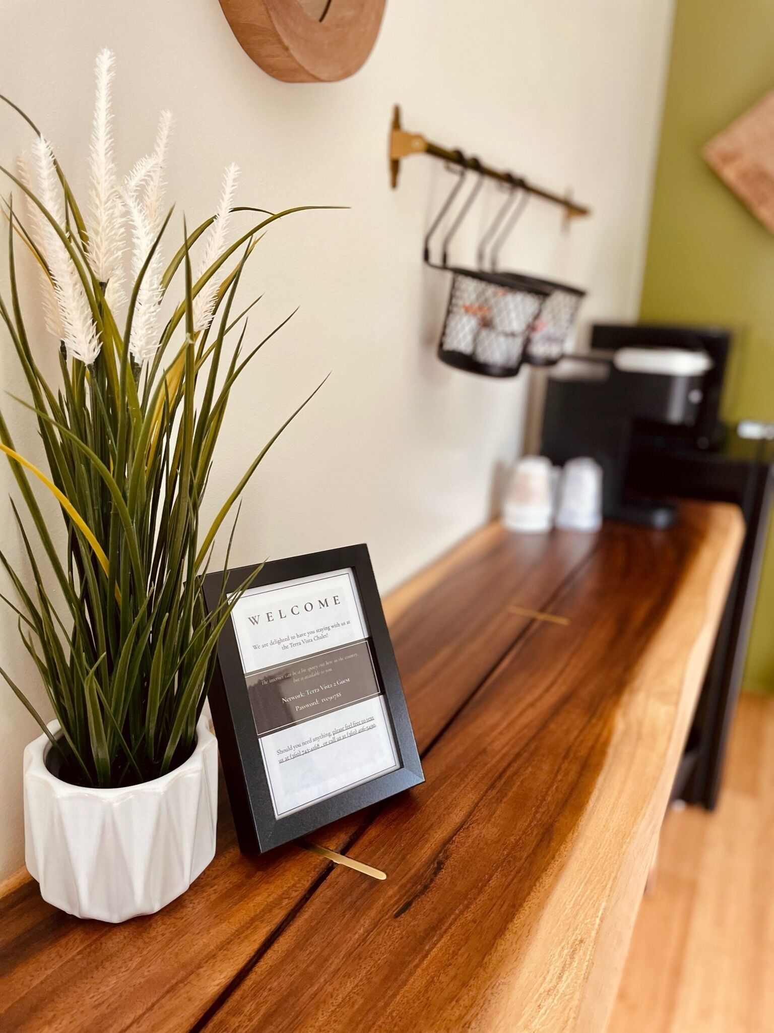 A reception desk with a welcome sign, a potted plant, and a coffee machine in the background.