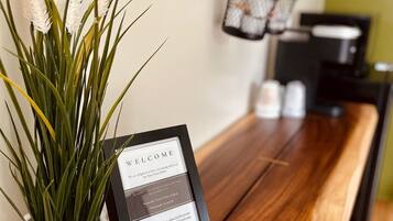 A reception desk with a welcome sign, a potted plant, and a coffee machine in the background.