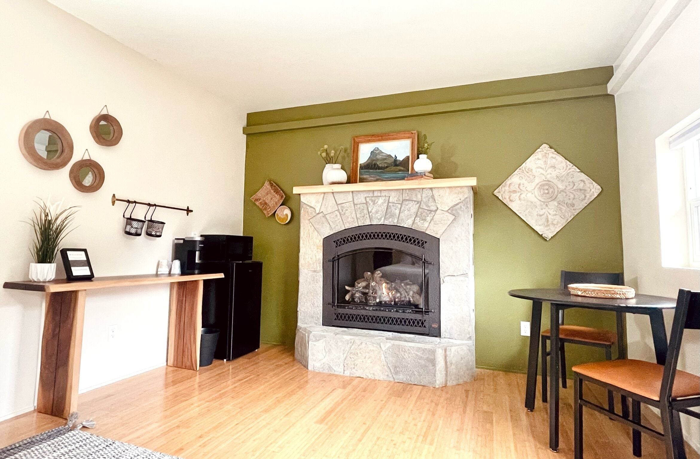 A living room with a stone fireplace, a coffee machine, a plant, and a dining area with a table and chairs.