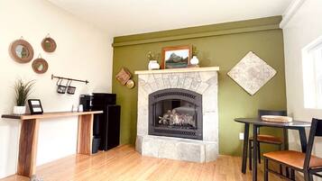 A living room with a stone fireplace, a coffee machine, a plant, and a dining area with a table and chairs.