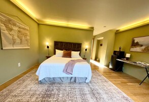 A bedroom with a large bed, two bedside lamps, a world map on the wall, and a desk with a plant.