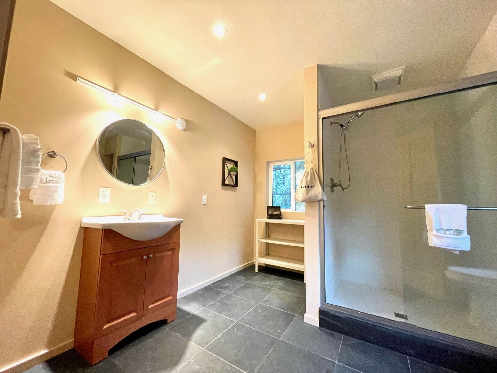 Un baño moderno con espejo redondo, tocador de madera y ducha con mampara de vidrio.