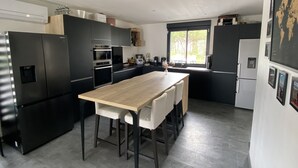 A modern kitchen with black appliances, a wooden dining table, and a large window. - Maison Individuelle Entre Océan et Forêt (Anglet)