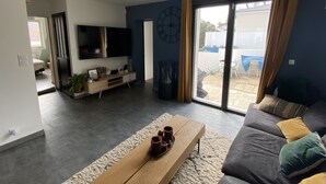 A modern living room with a flat-screen TV, a wooden coffee table, and a sofa with cushions. - Maison Individuelle Entre Océan et Forêt (Anglet)