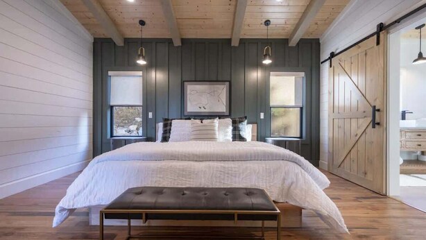 Un dormitorio con una cama grande, un banco, pisos de madera y una puerta de estilo granero.