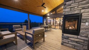 Una terraza exterior con mobiliario de madera, una chimenea de piedra y vista al océano.