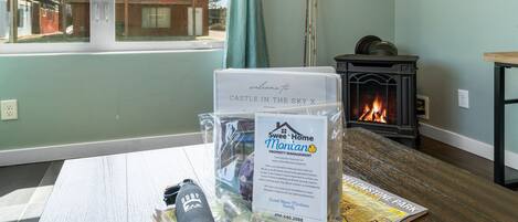 A room with a fireplace, a window with a view of a house, and a table with a welcome sign and a map.