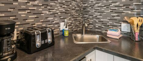 A modern kitchen with a tiled backsplash, a coffee maker, a toaster, a sink, and various utensils.