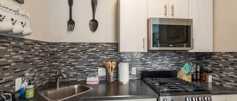 A modern kitchen with a stainless steel sink, a gas stove, and a microwave above cabinets.
