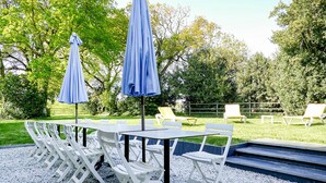 Ein Sitzbereich im Freien mit Tisch und Stühlen, umgeben von Bäumen und einem Kiesweg.