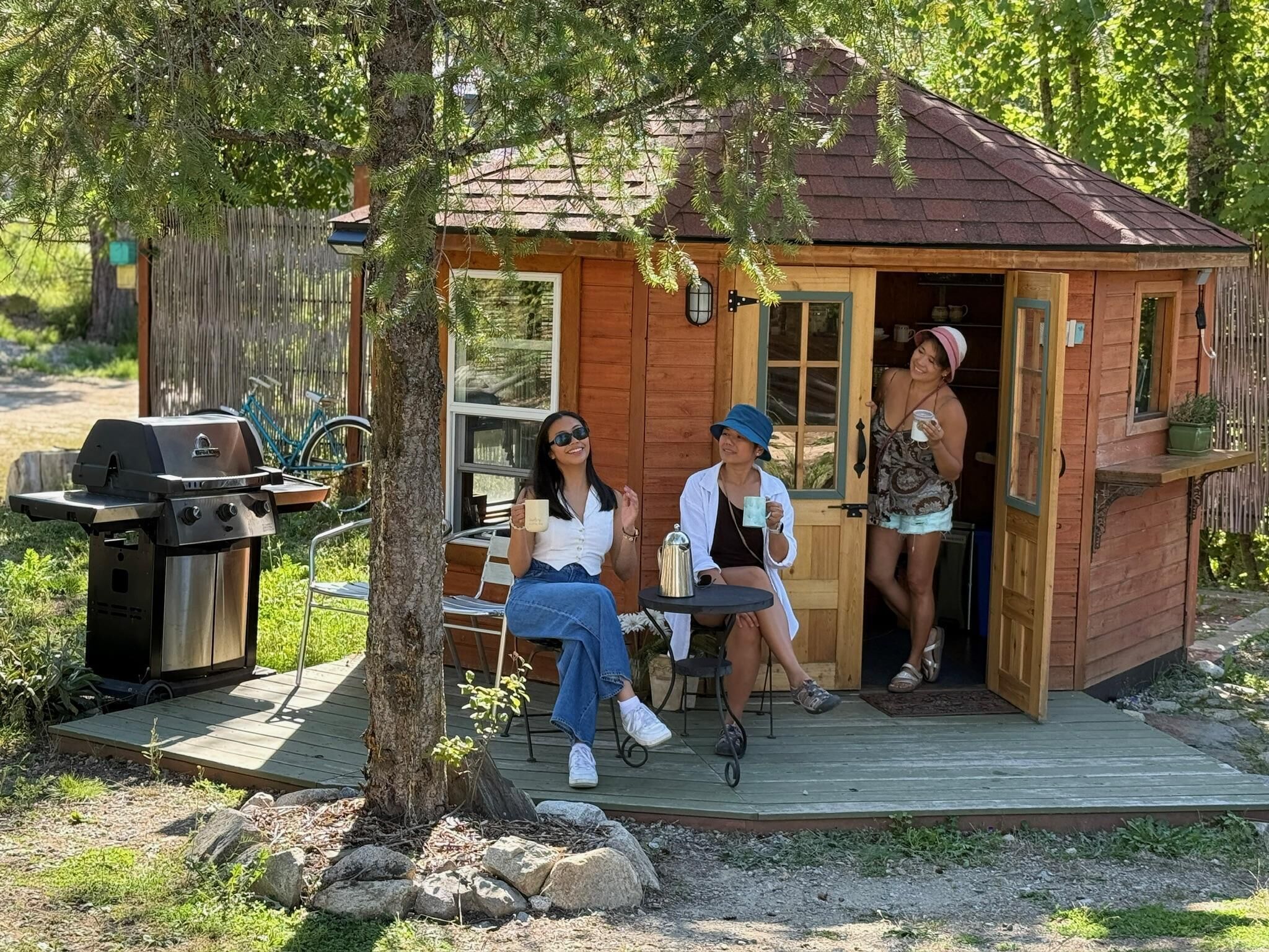 Una pequeña cabaña de madera con un balcón, una parrilla y una mesa con sillas.