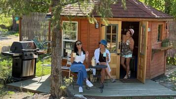 A small wooden cabin with a deck, a barbecue grill, and a table with chairs.