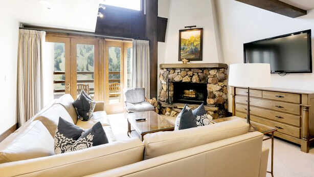 A living room with a stone fireplace, a sofa set, a television, and a large window with curtains.