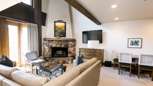 A living room with a stone fireplace, a sofa, a chair, a table, and a TV mounted on the wall.