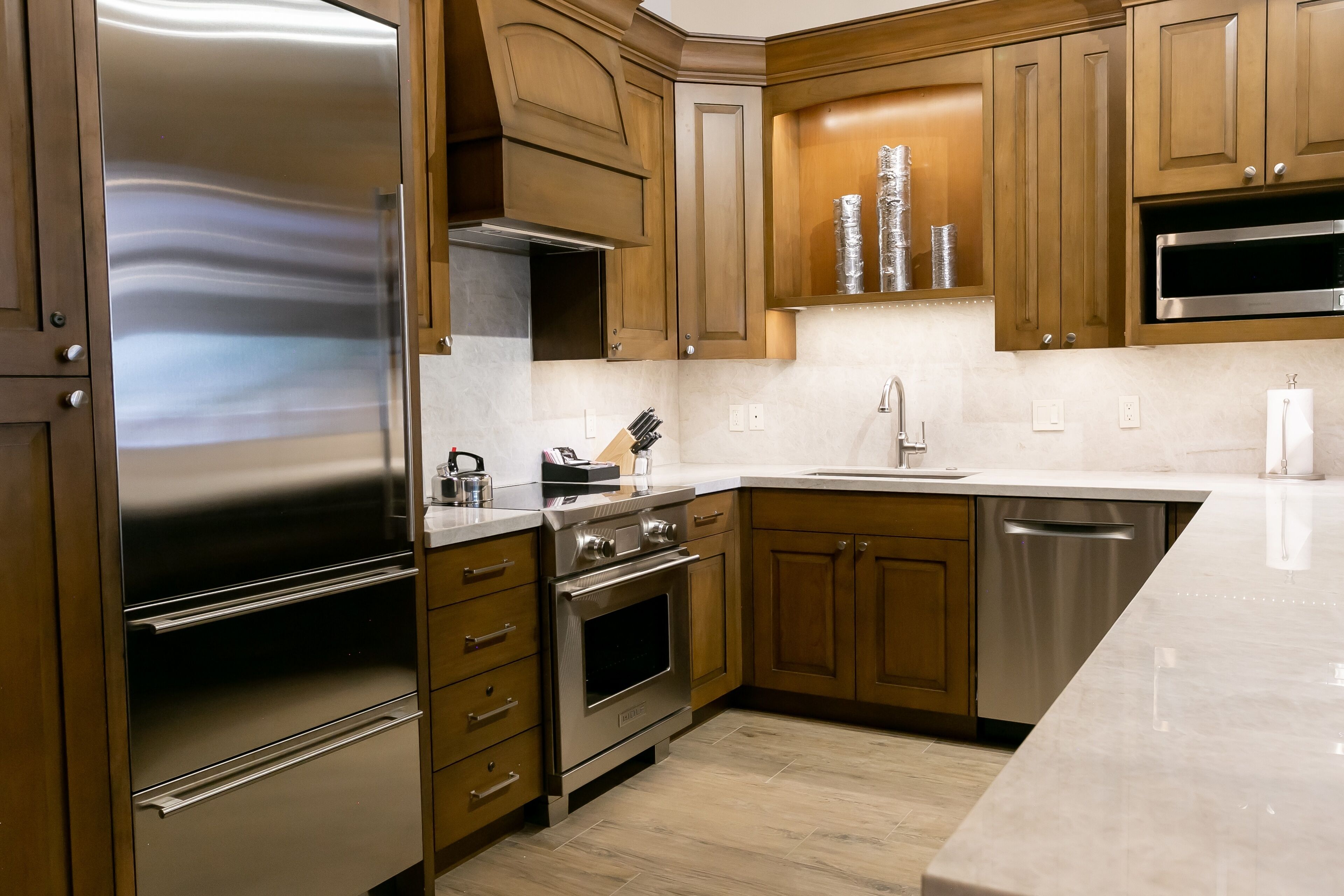 A modern kitchen with stainless steel appliances, wooden cabinets, and a marble countertop.
