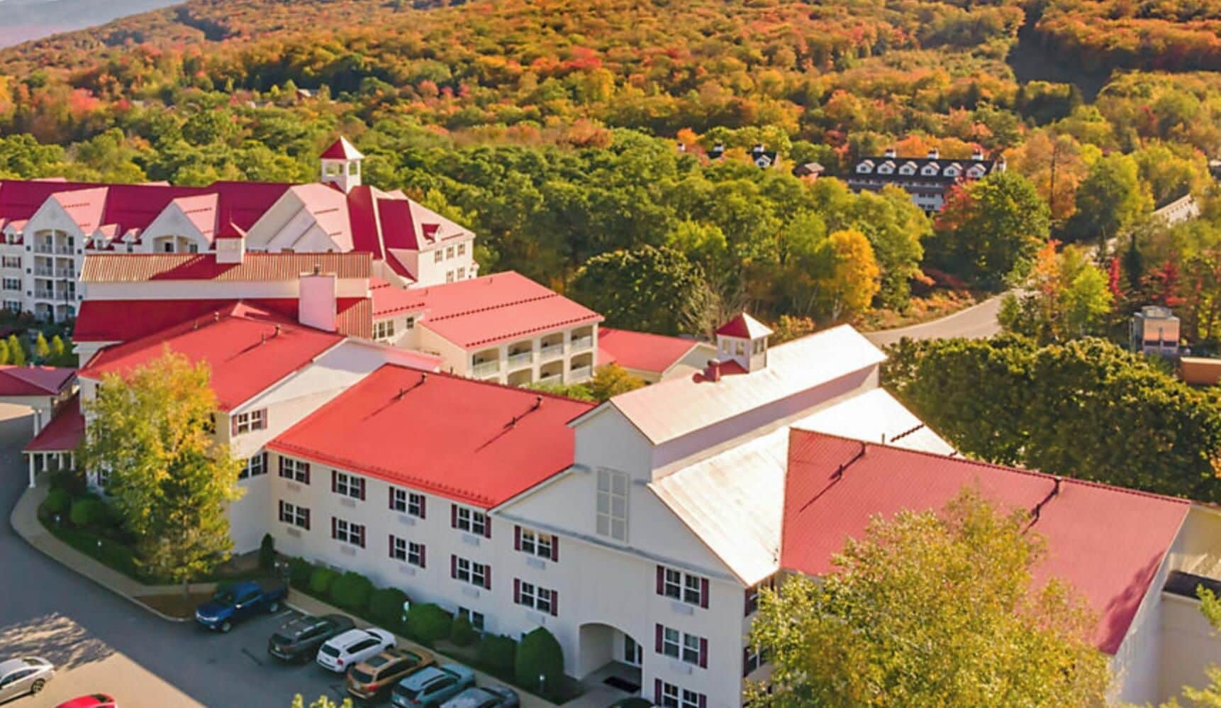 A large building with multiple red roofs, surrounded by trees and a hilly landscape.
