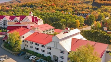 A large building with multiple red roofs, surrounded by trees and a hilly landscape.