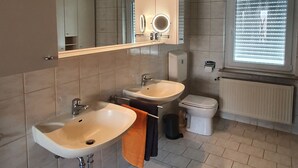 Une salle de bain moderne avec deux lavabos, un miroir avec éclairage intégré, des toilettes et un radiateur.