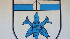 Un emblème en forme de bouclier, orné d’un poisson et d’une croix.