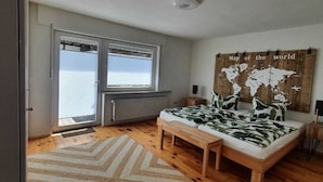 Une chambre à coucher avec un lit, un banc en bois, une fresque représentant une carte du monde et une fenêtre avec des stores.