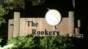 En träskylt med texten ”The Rookery”, omgiven av grönska och en flagga.