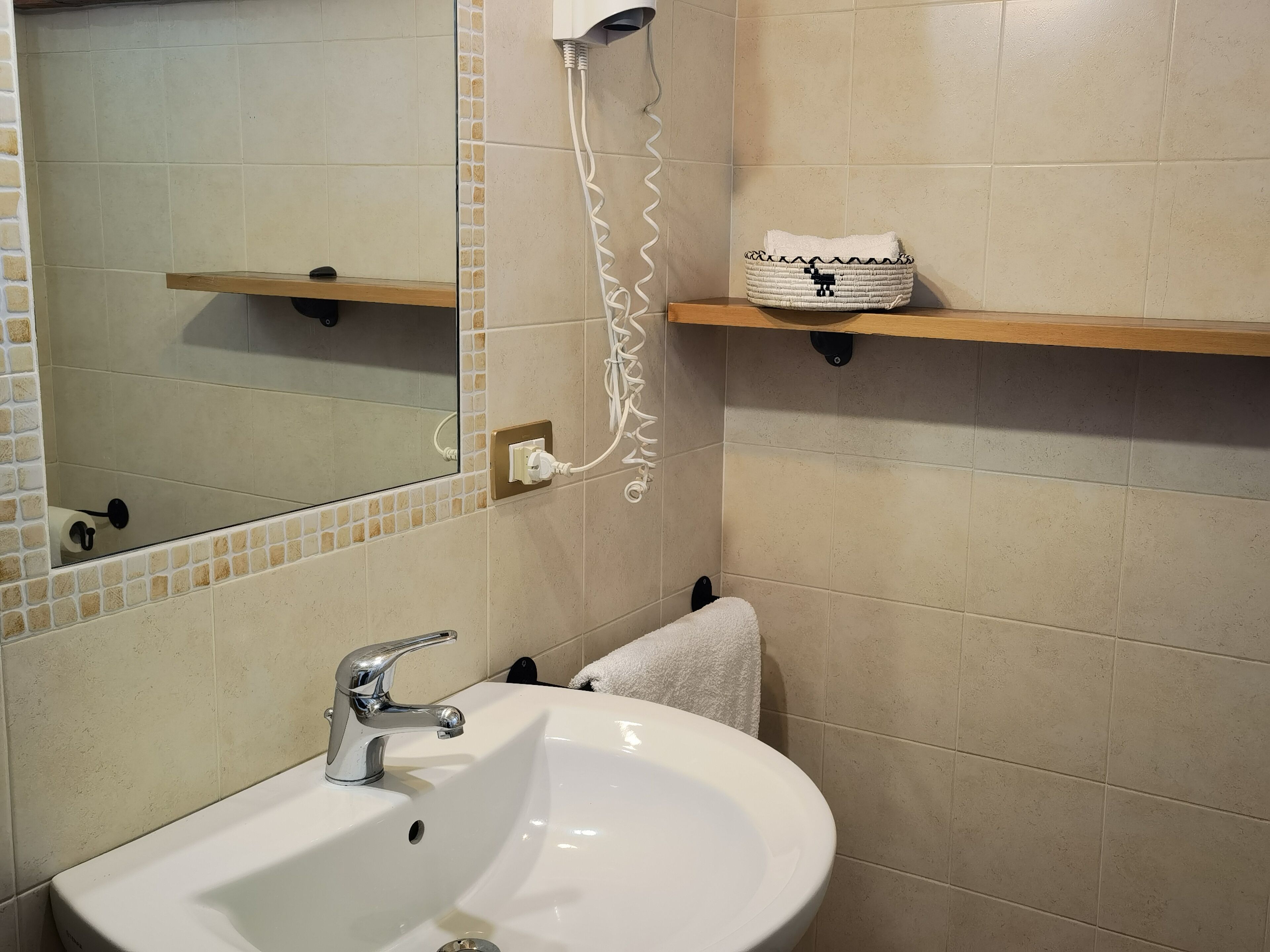 Un baño con un lavamanos blanco, un espejo, un perchero para toallas y una estantería con una cesta tejida.