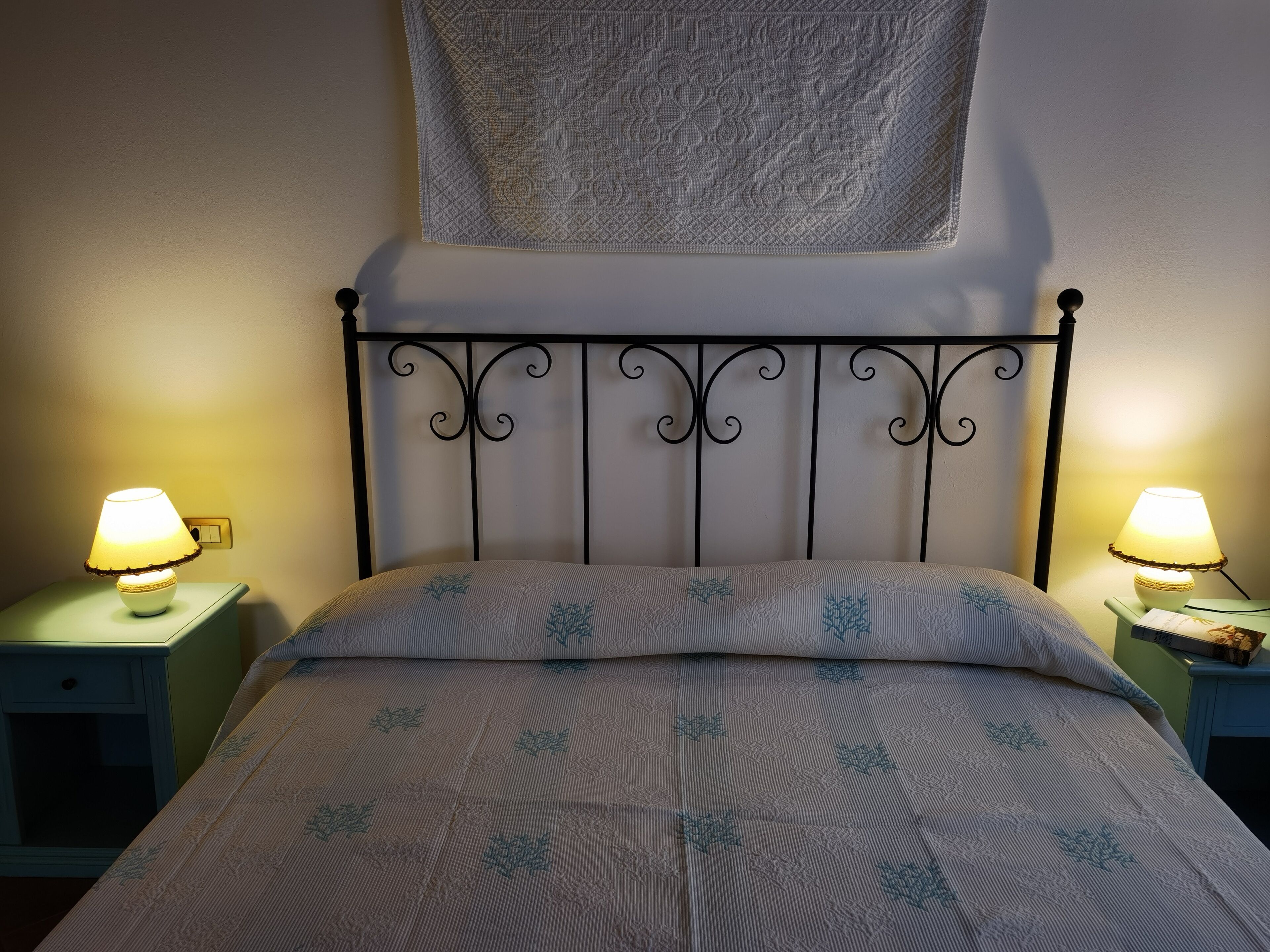 Ein Bett mit gemustertem Überwurf, zwei Nachttischlampen und einem dekorativen Wandbild darüber.