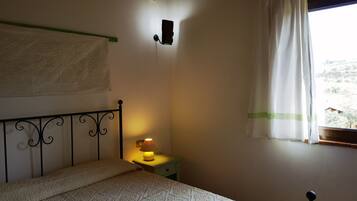 Un dormitori amb un llit, una làmpada de nit, una làmpada de paret, una finestra amb cortina i vistes a l'exterior.