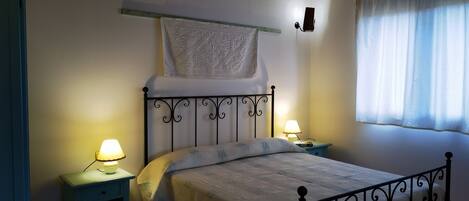 A bedroom with a bed, two bedside tables with lamps, a hanging tapestry, and a window with curtains.