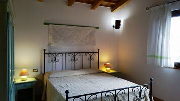A bedroom with a bed, two bedside tables, a wall-mounted shelf, and a window with curtains.