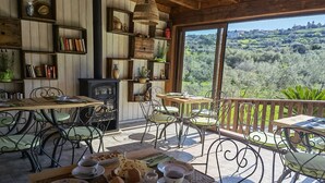 A cozy outdoor dining area with rustic wooden furniture, a large window offering a scenic view of a hilly landscape, and shelves with books and decorative items. - la corte degli ulivi (Tresnuraghes)