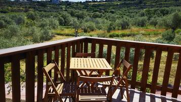 Eine Holzterrasse mit Tisch und Stühlen, die auf eine hügelige Landschaft mit Grünflächen und Gebäuden in der Ferne blickt.